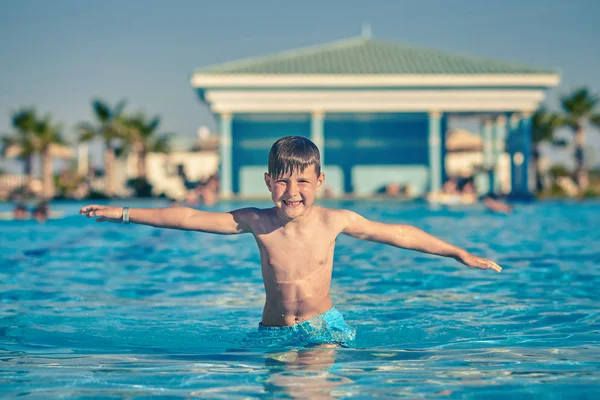 Gülümseyen beyaz çocuğun portresi tatil köyünde havuzda vakit geçiriyor. O, yaz tatilinin tadını çıkarıyor..