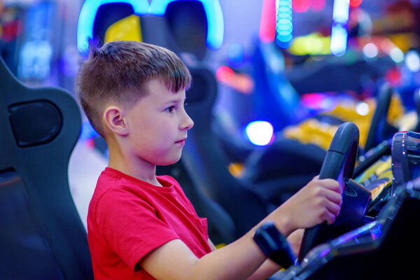 Indoor activity. European boy in red t-shirt playing racing simulator in play ground in shopping mall. He is enjoying his leisure time.