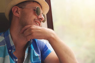 Güneş gözlüklü ve şapkalı gülümseyen yakışıklı adam trenle pencereden içeri bakıyor..