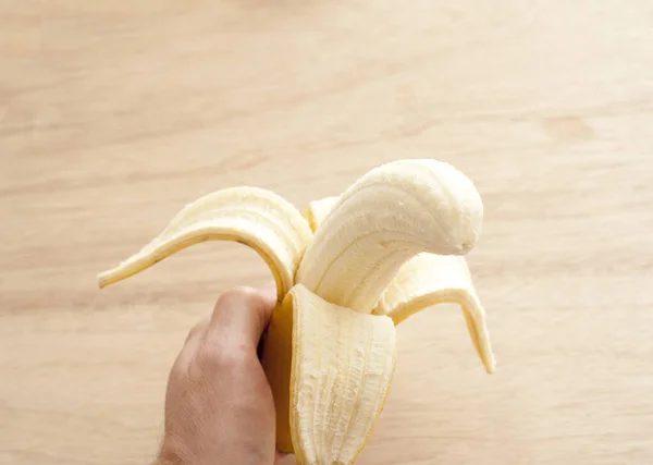 Man eating a ripe fresh banana holding it in his hand with half the skin peeled back to reveal the fruit, over a wooden background