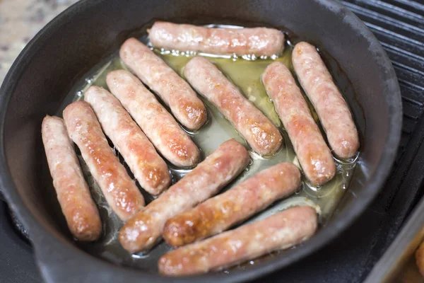 Pork sausages cooking on a griddle pan in their own juice viewed high angle