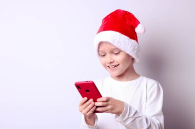 Akıllı telefonlu Noel Baba şapkalı bir çocuk.
