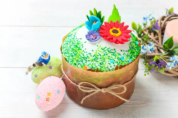 Easter cake with floral decorations and colored eggs on a white wooden background.