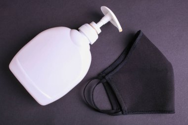 Yeniden kullanılabilir koruyucu tıbbi yüz maskesi ve siyah arka planda sıvı antibakteriyel sabun. Virüs salgınını algıla.