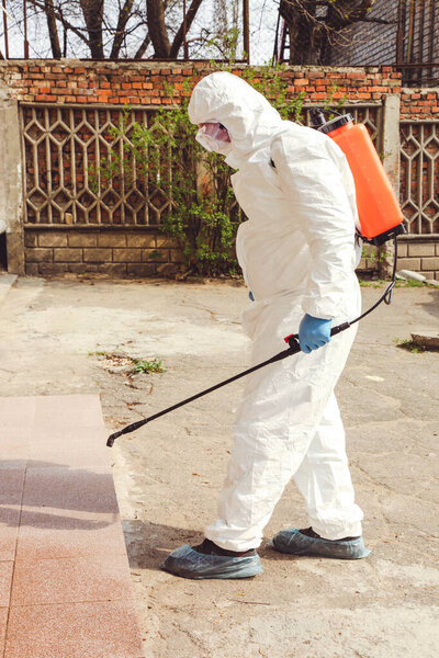 A specialist in a protective suit with a disinfection sprayer against coronavirus infection on the street. Epidemic control.