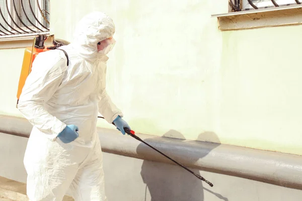 A specialist in a protective suit with a disinfection sprayer against coronavirus infection on the street. Epidemic control.