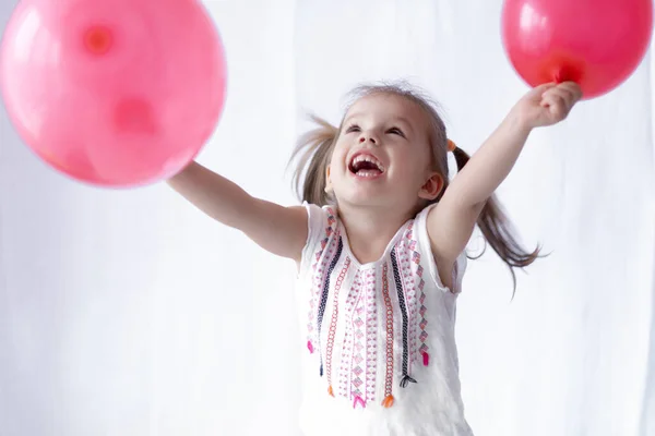 Vrolijke en vrolijke emoties van een meisje van twee jaar. Klein meisje houdt twee rode ballen in haar handen. mooi meisje spelen met ballonnen — Stockfoto