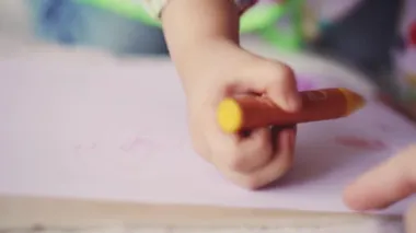 3 yaşındaki küçük kız bir kağıt parçasına pastel boyalarla resim çiziyor. Slav görünümlü güzel kız yatakta oturuyor.