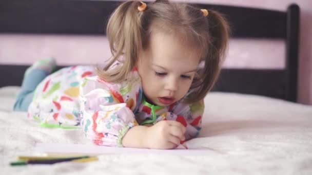 Kleines Mädchen von 3 Jahren malt auf ein Blatt Papier. Schöne Mädchen slawischen Aussehens malt auf dem Bett liegend — Stockvideo