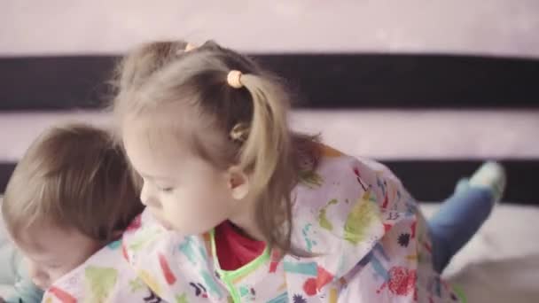 Les enfants jusqu'à trois ans dessinent des crayons couchés sur le lit. Frère et sœur dessinent sur un morceau de papier couché sur le ventre sur le lit 