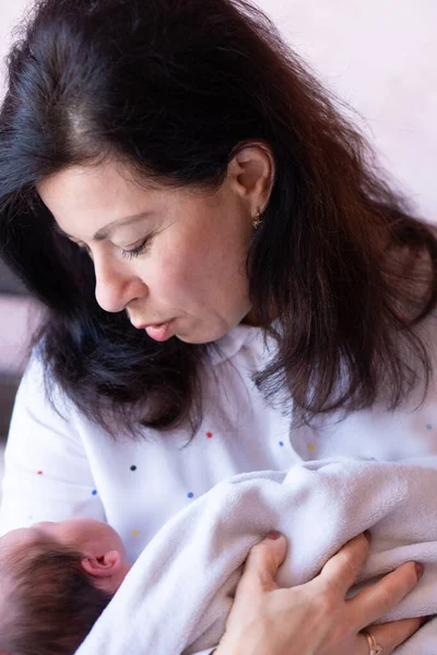 Nenek muda menggendong bayi sambil duduk di tempat tidur. Nenek muda yang cantik menghabiskan waktu dengan bayi yang baru lahir duduk di tempat tidur — Stok Foto