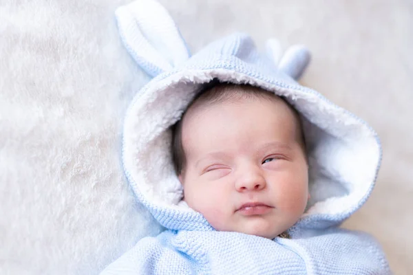 Closeup portrait of a sleeping newborn baby. Newborn wearing a warm blue jacket with toy bunny ears sleeping on blanket in sunny nursery.