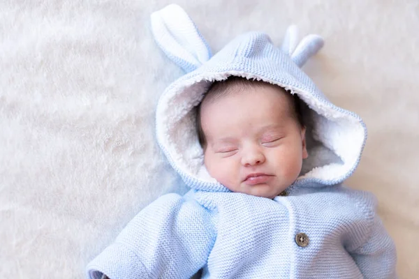 Uyuyan bir bebeğin yakın plan portresi. Yeni doğan, oyuncak tavşan kulaklı, sıcak mavi bir ceket giyiyor. Güneşli bebek odasında battaniyenin üzerinde uyuyor.. — Stok fotoğraf
