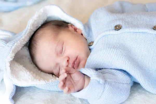 Close-up portret van een slapende pasgeboren baby. Pasgeborene draagt een warm blauw jasje met speelgoed konijnenoren slapend op deken in zonnige kinderkamer. — Stockfoto