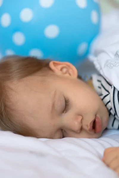 Klein blond baby is slapen in zijn bed op blauw bal achtergrond — Stockfoto