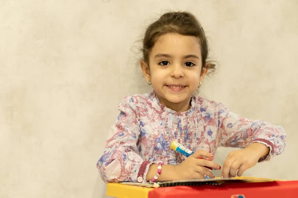 Klein meisje van Perzische verschijning tekent zittend aan het bureau. Mooi meisje van 4 jaar tekent met een waterpotlood. Perzisch meisje lacht — Stockfoto