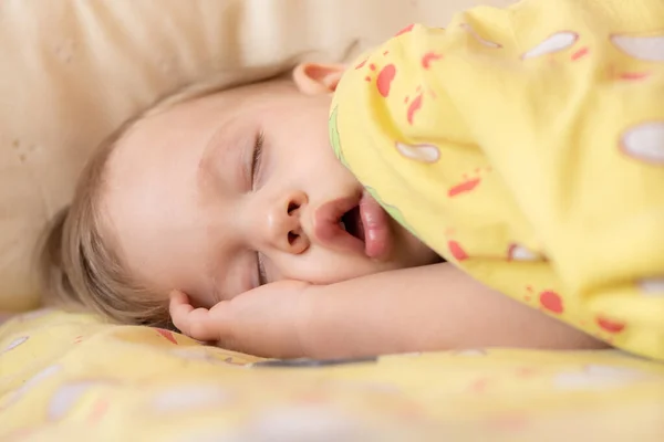 Een jongetje van twee slaapt alleen in een kinderbedje. De baby slaapt in de wieg met zijn hand onder zijn hoofd — Stockfoto