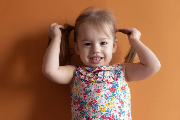 Portret van een mooi meisje van twee jaar op een oranje achtergrond. Emoties van een jong kind — Stockfoto