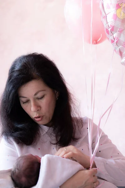 Nenek muda menggendong bayi sambil duduk di tempat tidur. Nenek muda yang cantik menghabiskan waktu dengan bayi yang baru lahir duduk di tempat tidur memegang balon di tangan — Stok Foto