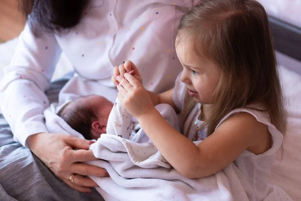 Menina segurando um bebê recém-nascido em seus braços. Irmã brincando com bebê recém-nascido enquanto sentado na cama — Fotografia de Stock