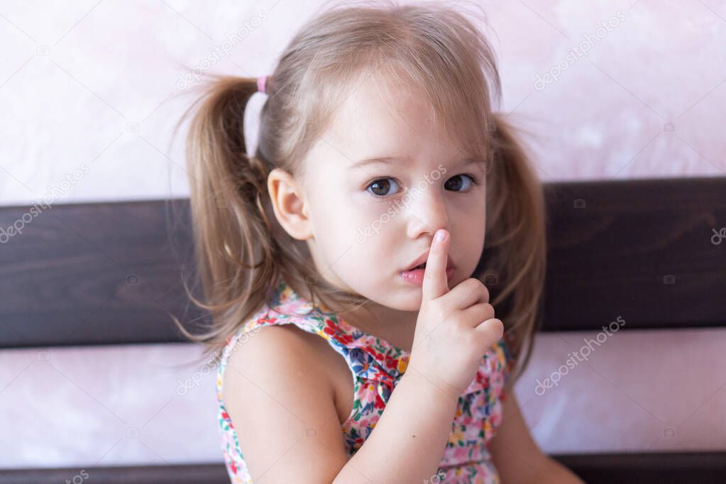 Little beautiful girl of 3 years shows a finger gesture quietly sitting on the bed