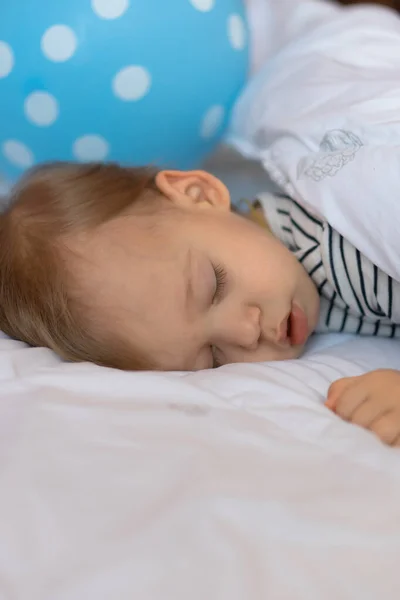 Klein blond baby is slapen in zijn bed op blauw bal achtergrond — Stockfoto