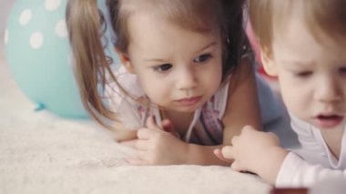 Erkek ve kız kardeşi 3 yaşın altında yatakta karnının üstünde çizgi film izliyorlar. Küçük çocuklar renkli balonların arasında bir yatakta uzanmış çizgi film seyrediyorlar.