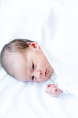 Yeni doğmuş. Bebek yatakta uyanık kalır. Yeni doğan bebeğin yakın plan portresi. Güneşli kreşte beyaz bir ceket giyen yeni doğmuş bir bebek..