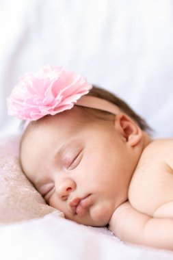tapılası bebek karnının üstünde uyuyor. Saçbandı olan yeni doğmuş bir bebek yumuşak bir battaniyenin üzerinde uyuyor.