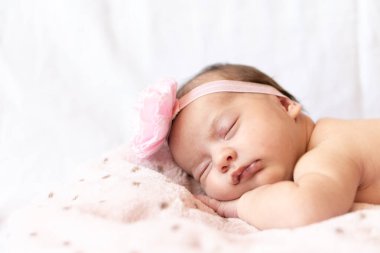 tapılası bebek karnının üstünde uyuyor. Saçbandı olan yeni doğmuş bir bebek yumuşak bir battaniyenin üzerinde uyuyor.