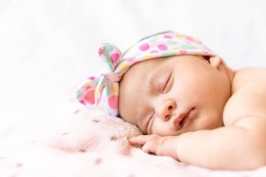 tapılası bebek karnının üstünde uyuyor. Saçbandı olan yeni doğmuş bir bebek yumuşak bir battaniyenin üzerinde uyuyor.