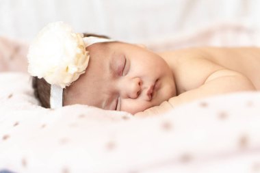 tapılası bebek karnının üstünde uyuyor. Saçbandı olan yeni doğmuş bir bebek yumuşak bir battaniyenin üzerinde uyuyor.