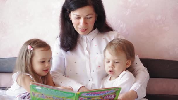 Avó e netos menino menina lê livro na cama. Mulher idosa, crianças — Vídeo de Stock