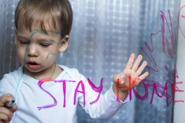 Sevimli küçük kız umut işareti olarak pencereye gökkuşağı çizimi yapıyor. Tecrit sırasında evde kalan çocuklar için yaratıcı oyunlar. Kişisel izolasyon ve koronavirüs karantina kavramı