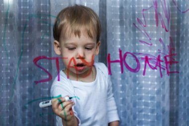 Adorable toddler girl attaching rainbow drawing to window glass as sign of hope. Creative games for kids staying at home during lockdown. Self isolation and coronavirus quarantine concept clipart