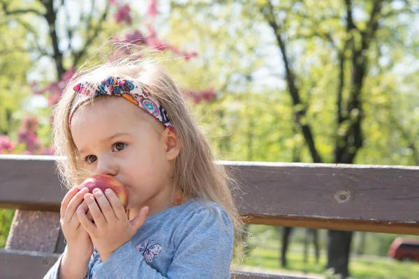 Tijd buiten doorbrengen. Mooi klein meisje met hoofdband in het voorjaar in het park. close-up uitzicht op kleine meisje dat is het eten van een appel — Stockfoto