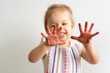 Resim çocuklar için eğlencelidir. Mutlu kız kirli ellerle oynar. Renkli resimde küçük kız ellerini gösteriyor. Küçük kız farklı duygular gösterir.