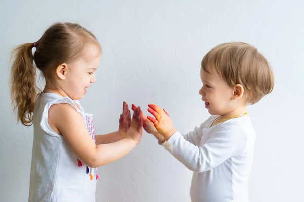 Malování je zábava pro děti - šťastné děti si hrají s barvou špinavýma rukama. Bratr a sestra si hrají s rukama na barevné malbě. Děti si hrají na dort — Stock fotografie