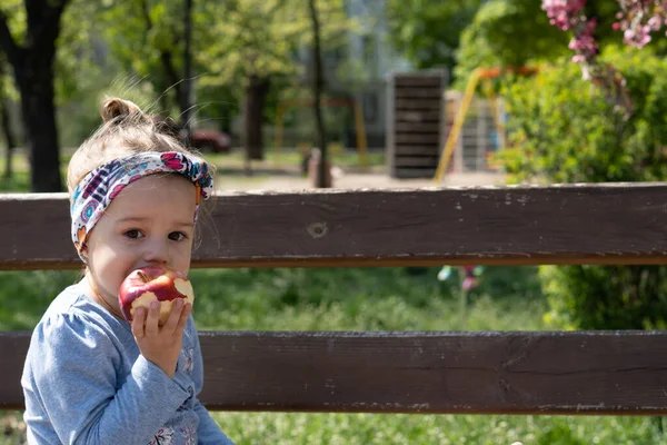 Tijd buiten doorbrengen. Mooi klein meisje met hoofdband in het voorjaar in het park. close-up uitzicht op kleine meisje dat is het eten van een appel — Stockfoto