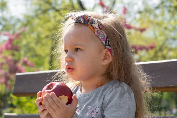 Tijd buiten doorbrengen. Mooi klein meisje met hoofdband in het voorjaar in het park. close-up uitzicht op kleine meisje dat is het eten van een appel — Stockfoto