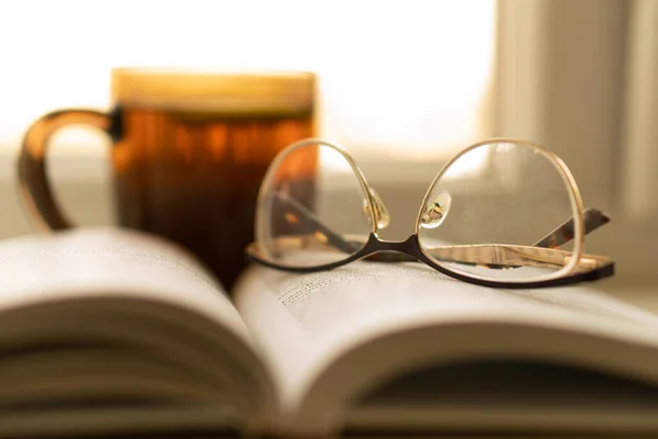 Isolation, loneliness, solitude, poetry, bookbinder, tea party concept. Black mug of warm tea with lemon and open book on the windowsill. Glasses on the opened book — Stock Photo, Image