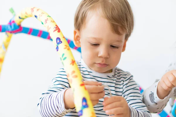 Pequeño chico guapo de 2 años jugando con juguetes sentados en la cama en el interior. Juguetes musicales que desarrollan habilidades motoras y pensamiento —  Fotos de Stock