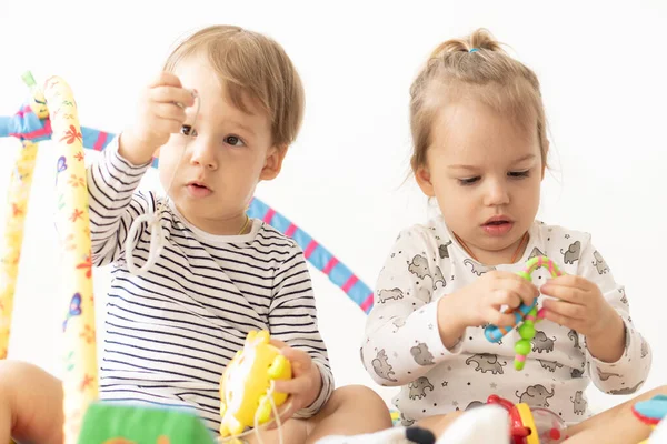 Deux jeunes enfants jouent avec des jouets assis ensemble sur le lit. Frère et sœur jouent avec des jouets colorés. Les enfants avec une petite différence d'âge jouent ensemble à l'intérieur. Jouets musicaux qui développent le moteur — Photo