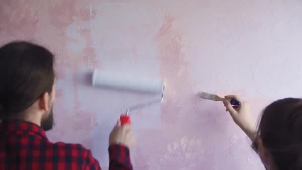 Прекрасна пара прикрашає своє нове приміщення і огорожу. Чоловік і дружина малюють стіну з роллерами, які занурюються в світло-синій фарби. Вони щасливі і веселяться. Відновлення вдома — стокове відео