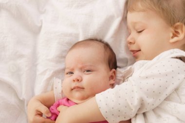 İki çocuk yatakta uzanıp kucaklaşıyor. Ağabeyi yerde yatıyor, sarılıyor ve yeni doğmuş kardeşinin elini tutuyor. Çocukluk ve aile kavramı