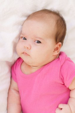 Küçük bebek beyaz bir yatakta karnının üstünde yatıyor. Yeni doğan uyandı ve etrafına bakıyor. Pembe elbiseli yeni doğmuş bebek gülümsüyor. Yeni doğan bebeğin tuhaf bakışı