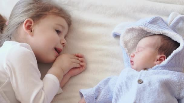 Infância, infância, família, sono, conceito de descanso - close-up de duas crianças, bebê recém-nascido e menina de três anos dormindo juntos em uma cama bege e branca. Irmãs estão dormindo no sofá em casa . — Vídeo de Stock