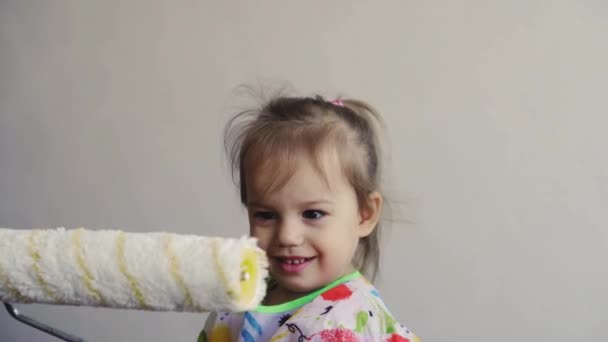 Repair, renovation, home, family, childhood, parenthood, fatherhood, self-isolation, quarantine concept - close-up little 3 years old girl playing with roller, painting wall in apartment white paint. — Stock Video