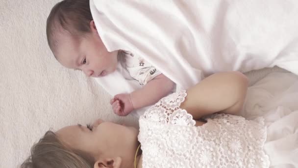 Kindertijd, kindertijd, ouderschap, moederschap, familieconcept - close-up van een pasgeboren baby en een ouder zusje liggend op een wit beige bed hand in hand. Twee zussen spelen op de bank. — Stockvideo