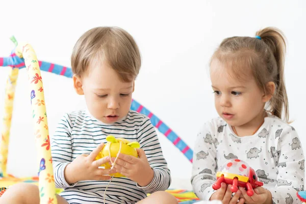 两个小孩坐在床上玩玩具。兄妹玩彩色玩具。年龄差异小的儿童一起在室内玩耍。开发马达的音乐玩具 — 图库照片